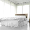 A white ruffled elastic bed skirt is shown beneath a bed in a bright, modern bedroom.