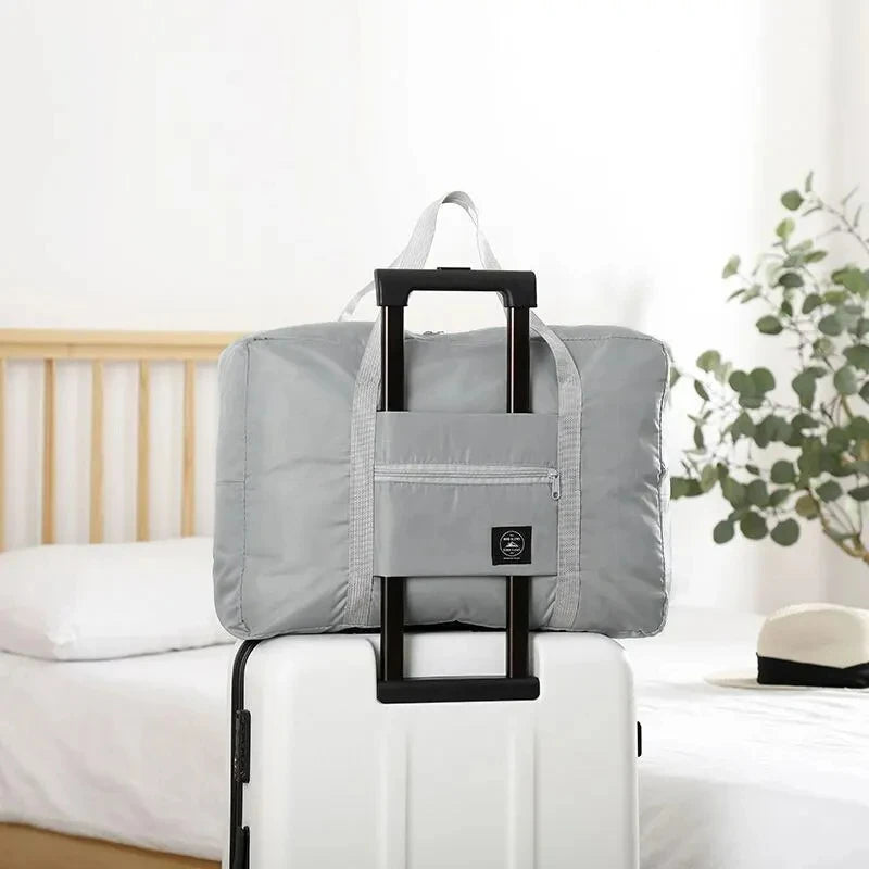 A gray foldable travel duffel bag with black handles resting on a white suitcase.