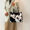 A woman holds a black and white faux fur leopard print tote bag in front of her while wearing a cream blazer.