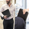 A man in a white shirt and black pants is holding a black laptop sleeve while standing near a window.