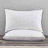 A white luxury goose down and feather pillow with a brown trim resting on a gray fabric.