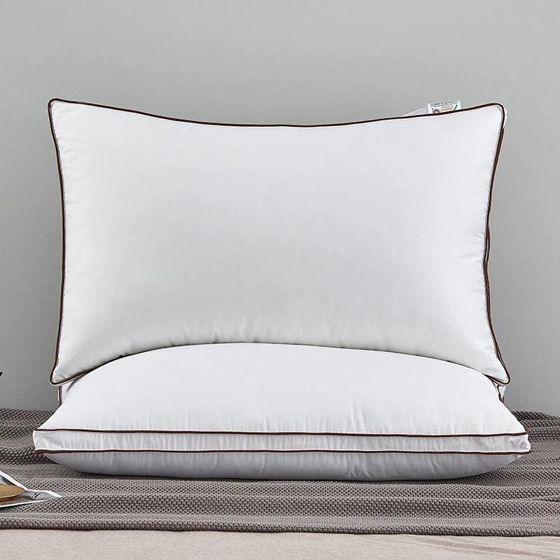 A white luxury goose down and feather pillow with a brown trim resting on a gray fabric.