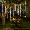Curtain fairy lights with warm white LEDs hanging from a tree branch in a nighttime outdoor setting.