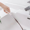 A hand is using a silicone drain clog remover and hair catcher tool to clear a sink drain.