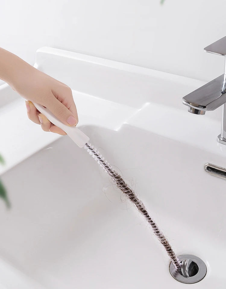 A hand is using a silicone drain clog remover and hair catcher tool to clear a sink drain.