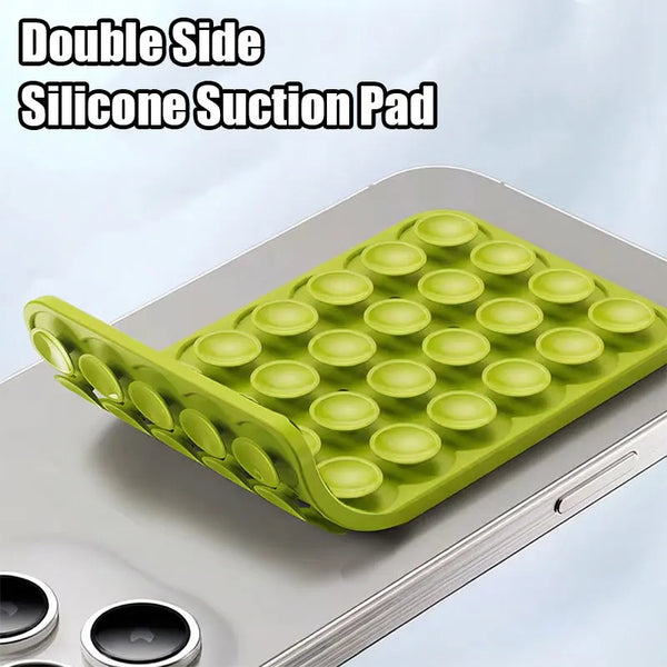 A green silicone suction pad with multiple cups is placed on a silver smartphone mount.