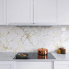A kitchen countertop featuring white cabinets, a stainless steel hood, and a backsplash with gold marble-patterned wallpaper.
