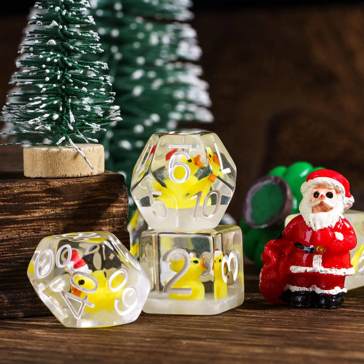 A set of clear resin dice featuring animal figures and numbers, displayed in front of a green Christmas tree.