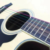 Close-up of a light-colored acoustic guitar showing six color-coded strings being tuned.