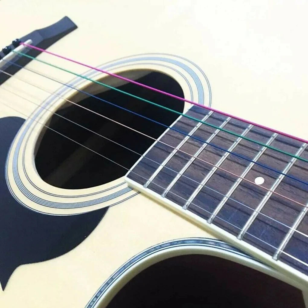 Close-up of a light-colored acoustic guitar showing six color-coded strings being tuned.
