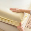 A hand is holding up a yellow fitted sheet to show its deep pocket and elastic band.