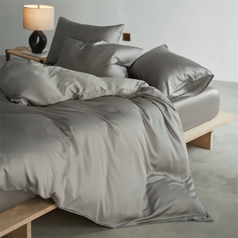 A luxury mulberry silk duvet cover set in a soft gray color displayed on a bed.