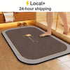 A brown diatomite bath mat with a gold trim is placed on a tiled bathroom floor.