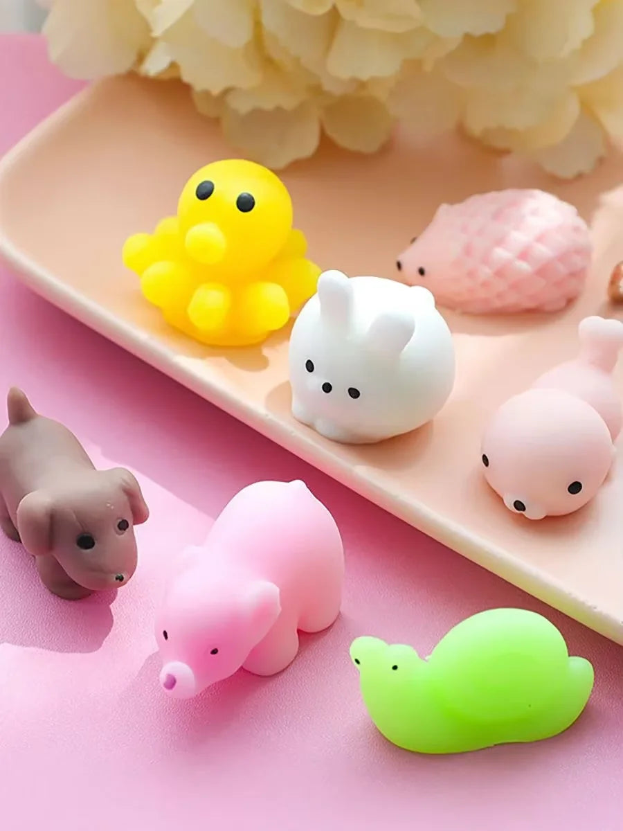 A collection of colorful, squishy animal stress relief toys including yellow, white, pink, and green figures on a light pink 