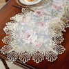 A lace table runner featuring a floral pattern in pink and gray on a dark wood table.