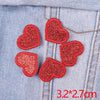 A set of five red glitter heart iron-on embroidered patches placed on a blue denim fabric.