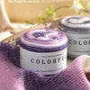 A purple and white yarn skein labeled Colorful Long distance cake BA is displayed on a wooden surface with soft lighting.