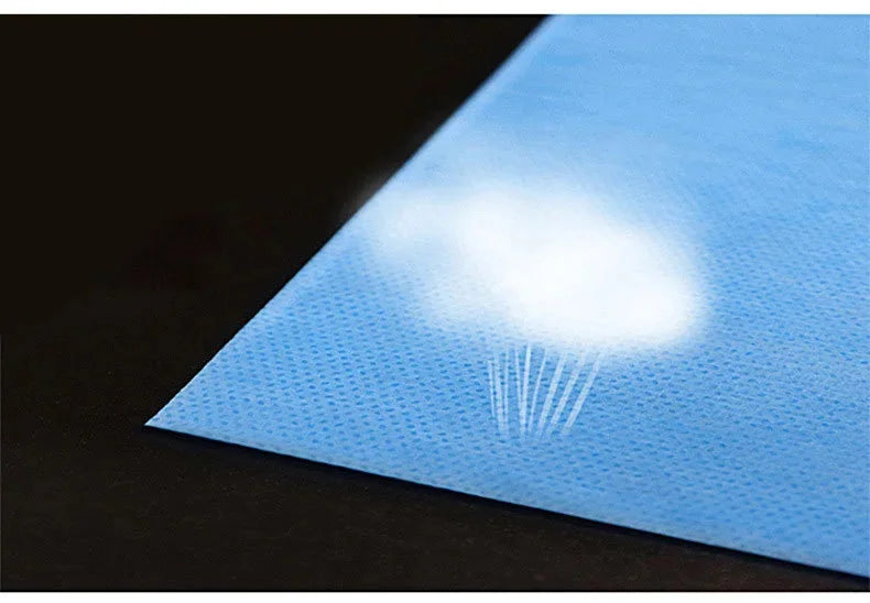 A sheet of light blue disposable bed linen with a bright white cloud pattern is shown on a dark surface.