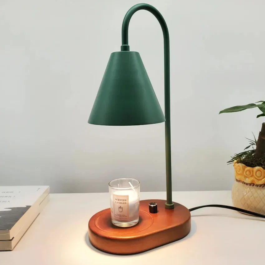 A tall, dark green electric candle warmer lamp with a curved neck and conical shade sits on a wooden base.