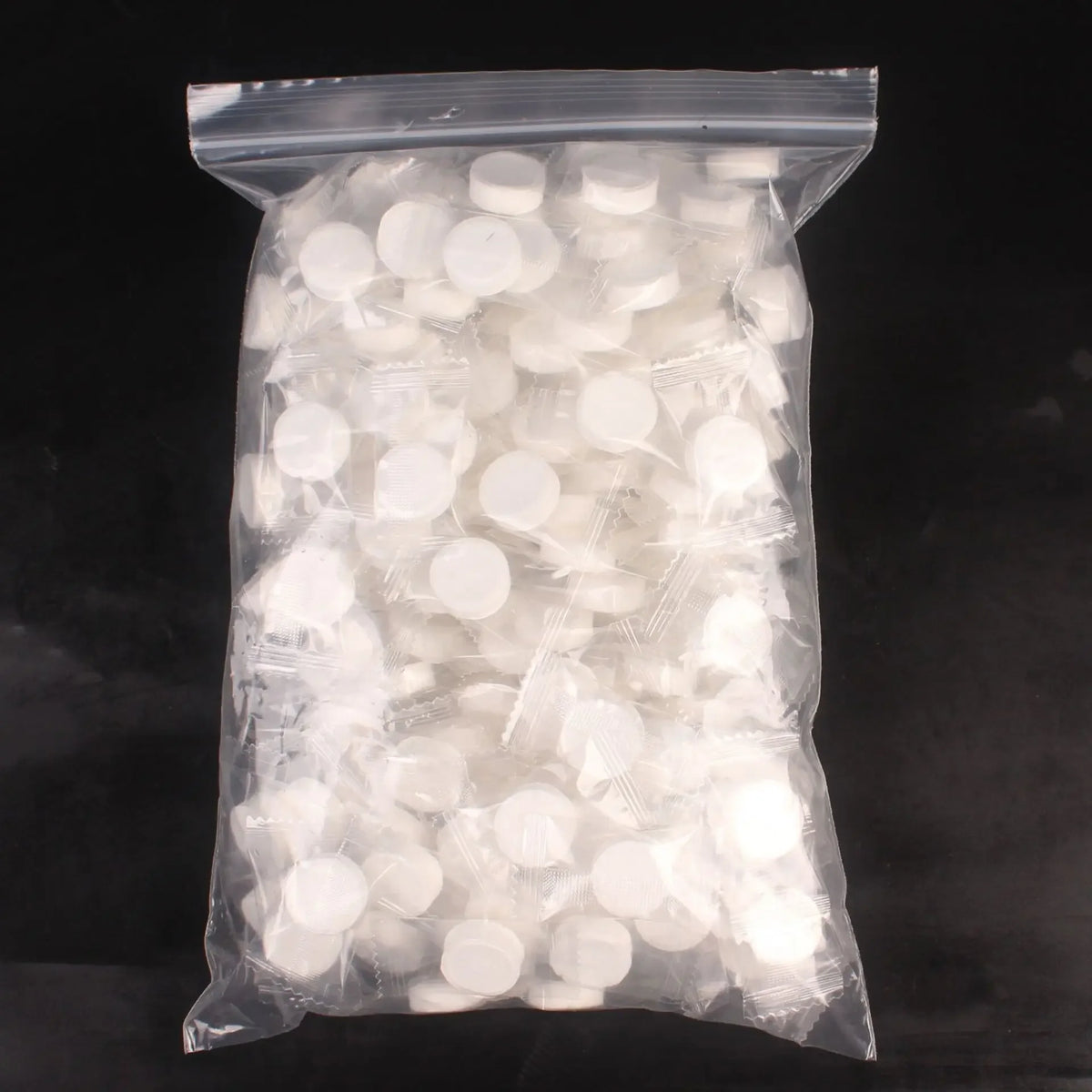A clear plastic bag filled with numerous white, compressed cleansing towels.