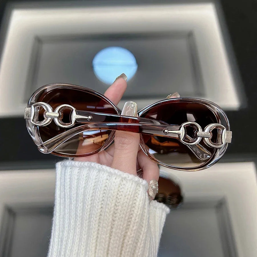 A hand holds a pair of brown tinted square vintage sunglasses against a light background.