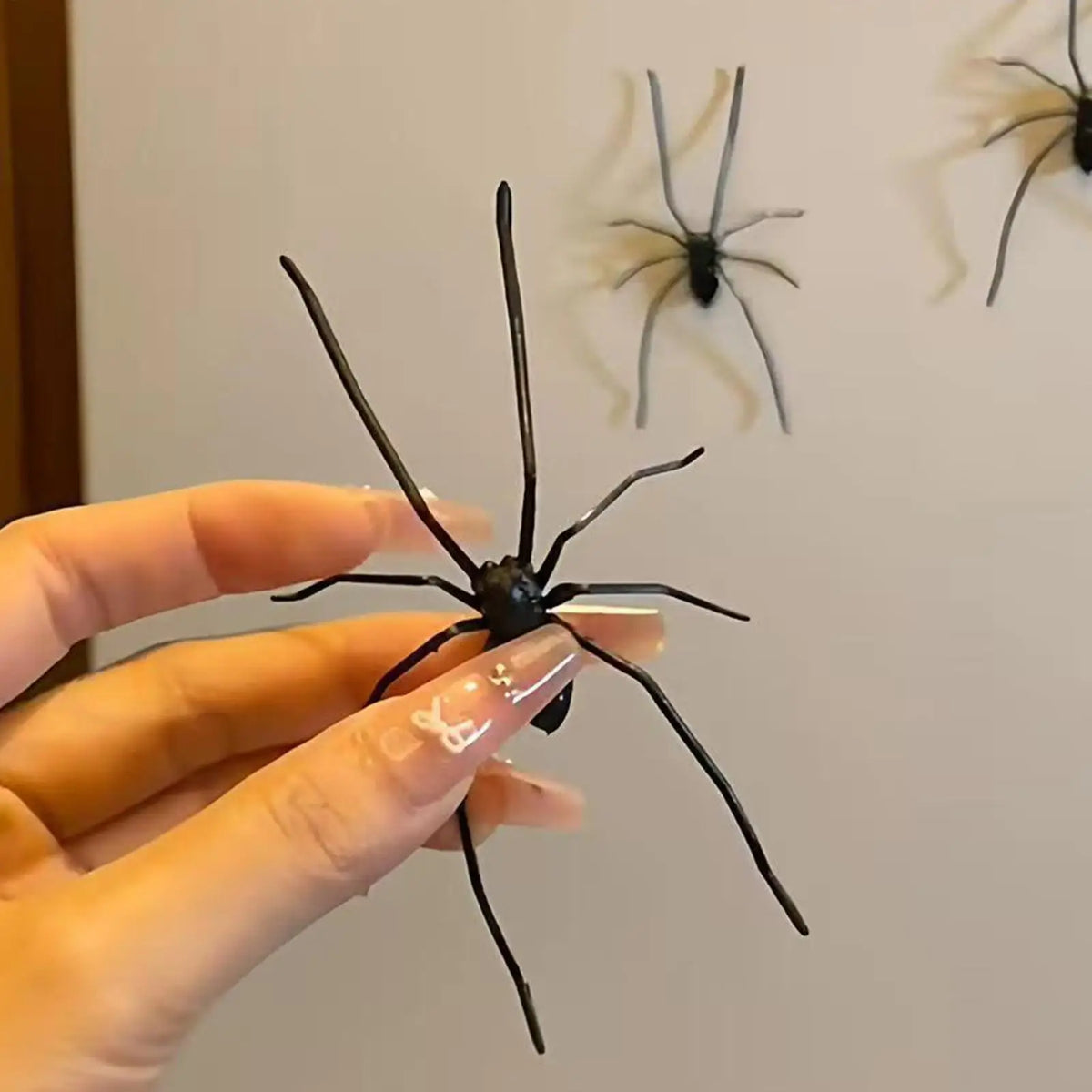 A hand holds a realistic black spider, which is a fridge magnet for funny prank decor.
