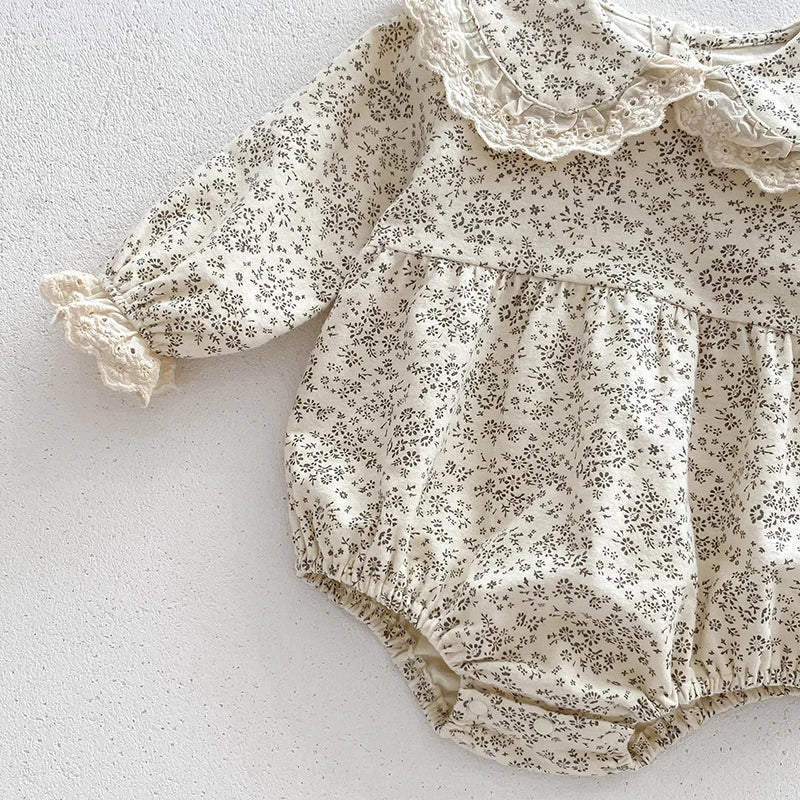 A light floral print cotton romper for a baby girl with delicate lace trim and ruffle details.