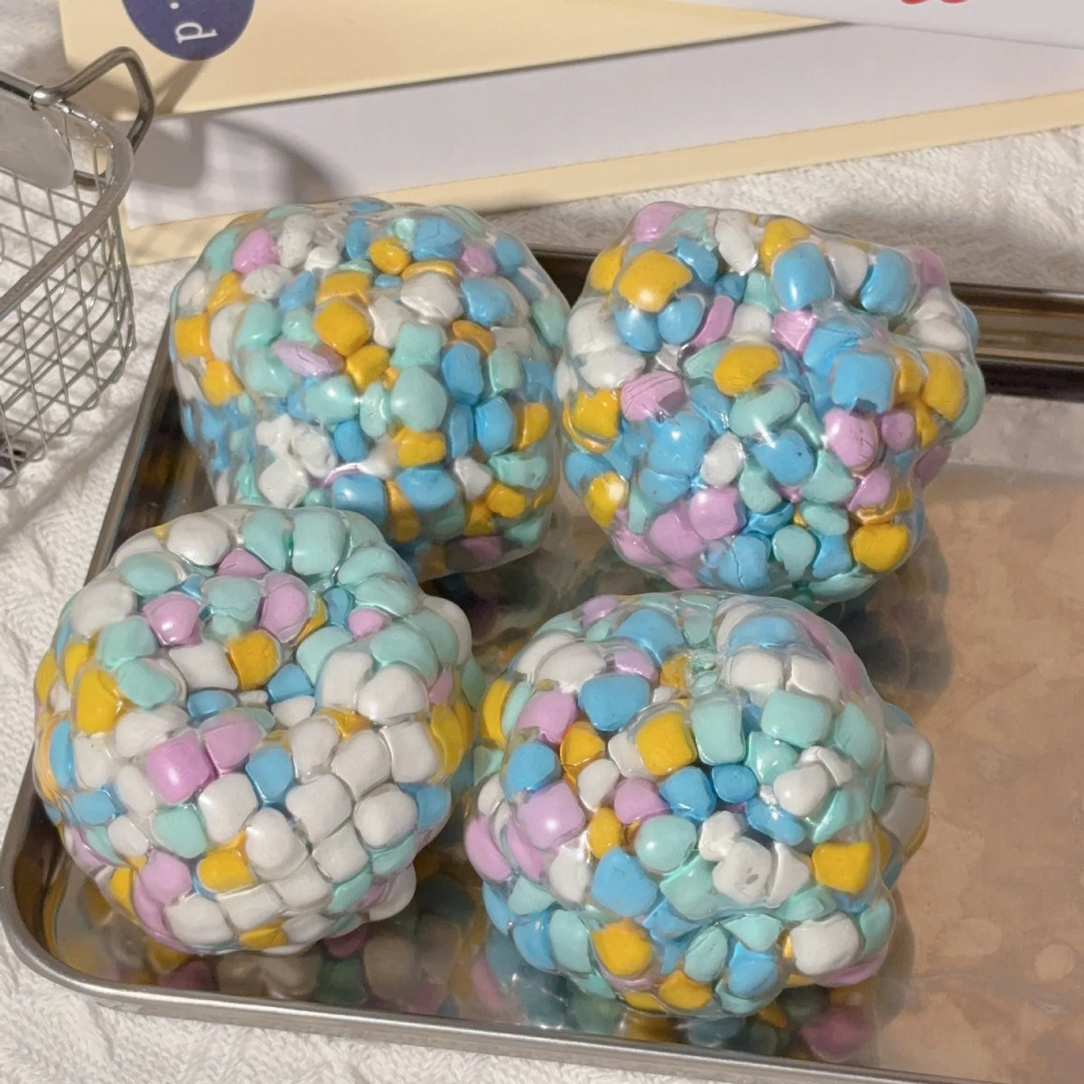 A collection of colorful squishy stress balls in various pastel shades are displayed on a tray.