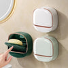 A wall-mounted soap holder with a lid and drainage in white and dark green colors.
