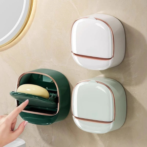 A wall-mounted soap holder with a lid and drainage in white and dark green colors.