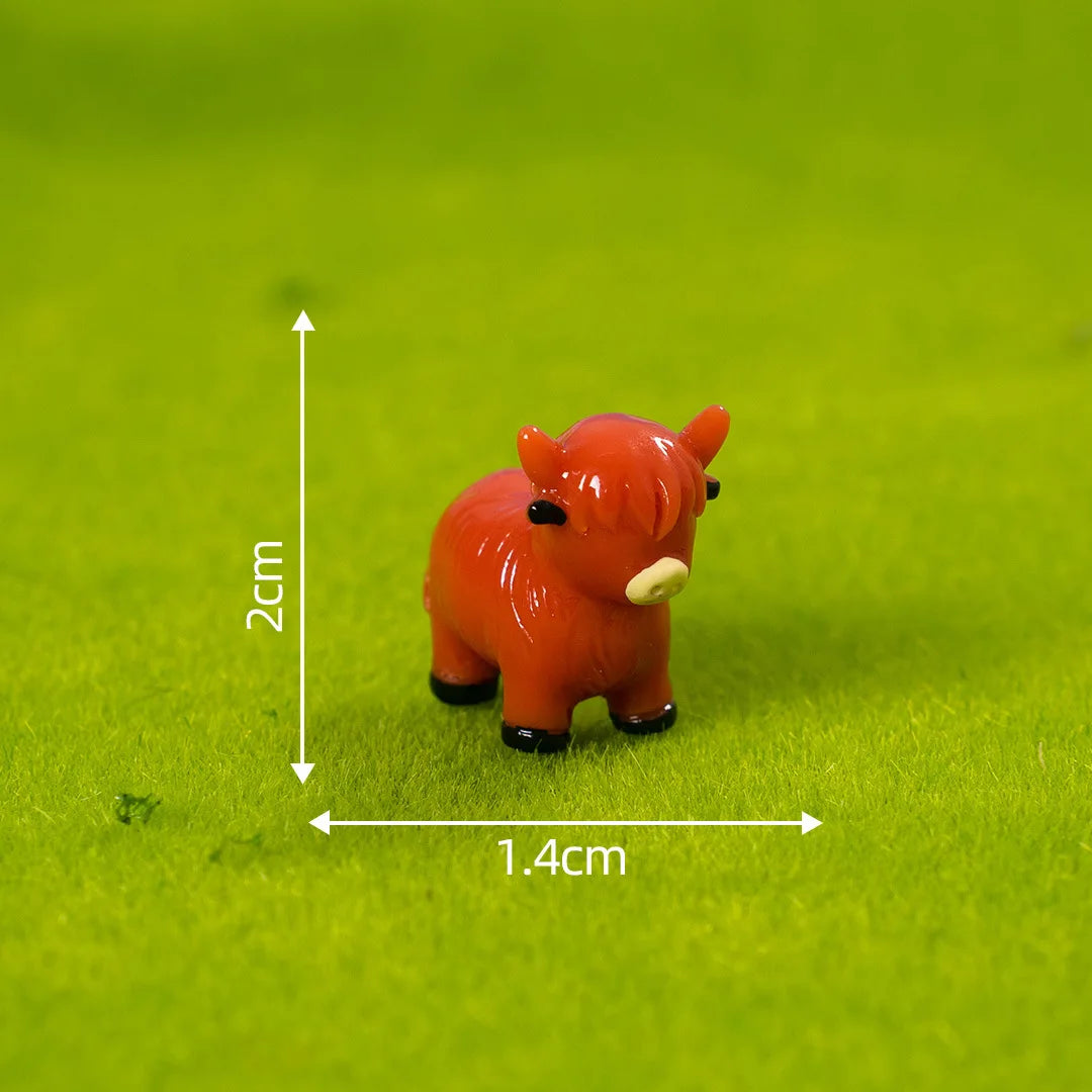 An orange resin figurine of a Highland cow, measuring 2cm high and 1.4cm wide, resting on green moss.