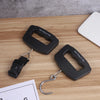 A black portable digital luggage scale is shown on a wooden surface with a hanging hook and a scale display reading Max: 50kg