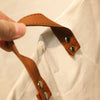 A hand is holding a brown leather strap with metal rivets, showing a detail of a folding cartoon print baby storage basket or