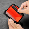 A hand is opening a black compact RFID wallet with an orange lining to reveal a credit card.