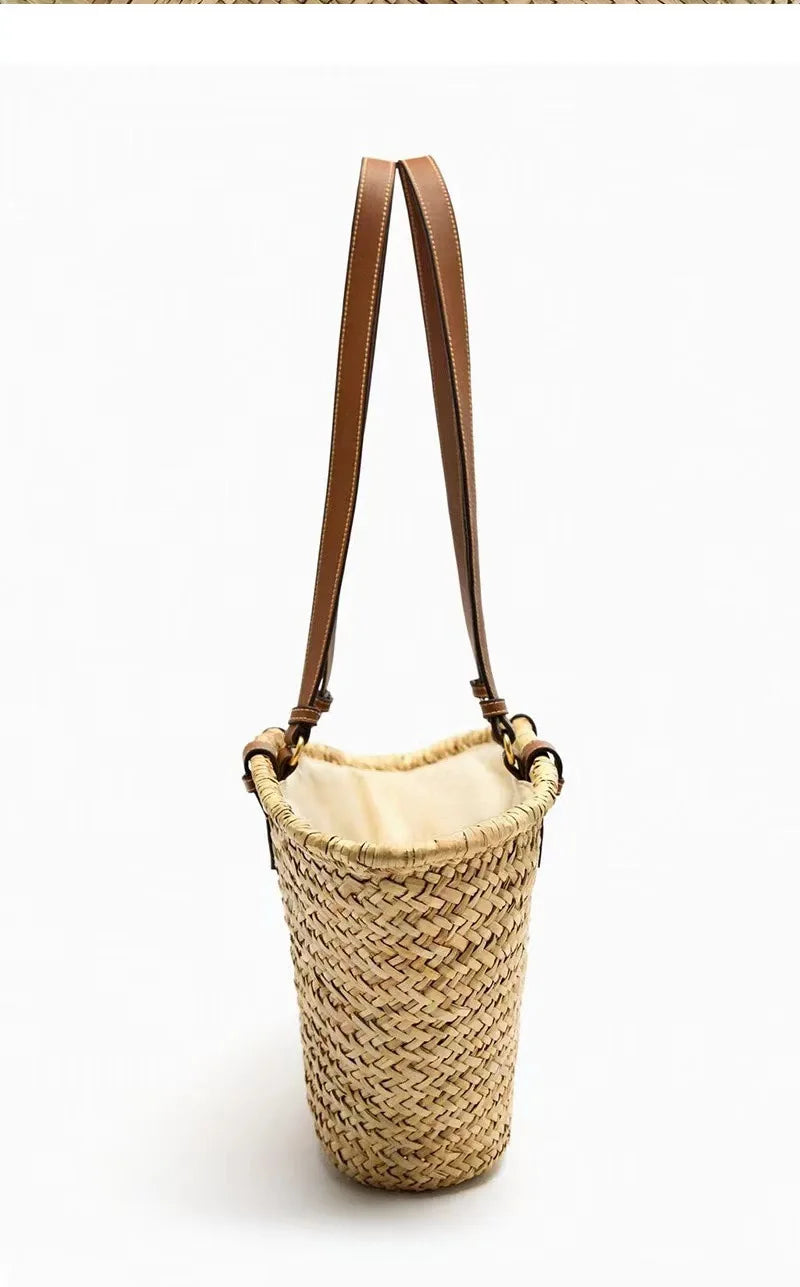 A handwoven straw tote bag with brown leather straps, shown against a white background.