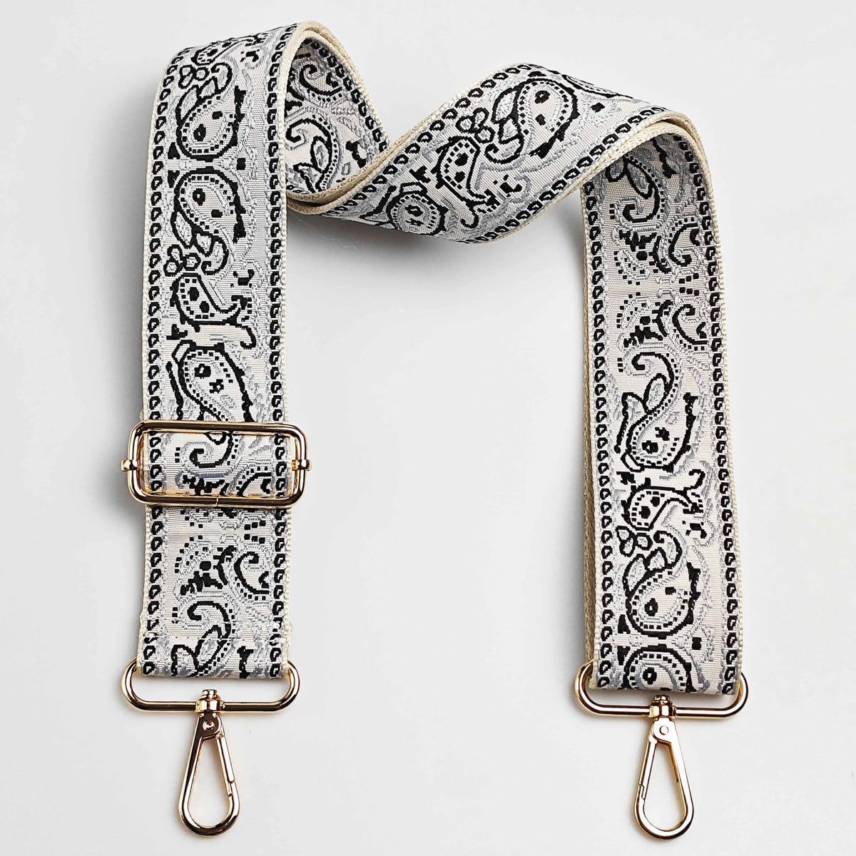 A beige and black paisley jacquard bag strap with gold-toned hardware.