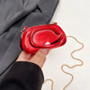 A hand holds a red mini clutch bag with gold chain strap against a gray blazer.