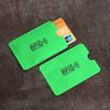 A bright green RFID protection card sleeve lying on a dark brown textured surface next to an orange identification card.