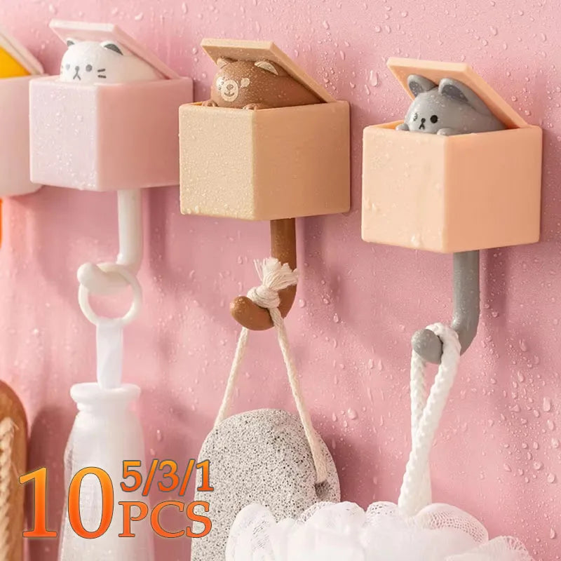Five adorable cat-shaped adhesive hooks in pink and beige are displayed against a pink textured wall.