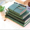 A stack of green leather refillable journals with a leather clasp resting on a white surface.