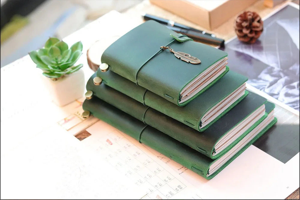 A stack of green leather refillable journals with a leather clasp resting on a white surface.