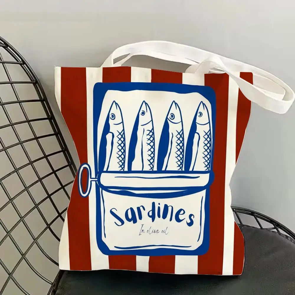 A canvas tote bag featuring a blue illustration of sardines in a rectangular frame on a striped background.