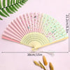 A pink and green vintage lace folding hand fan with a durable handle displayed on a light purple background.
