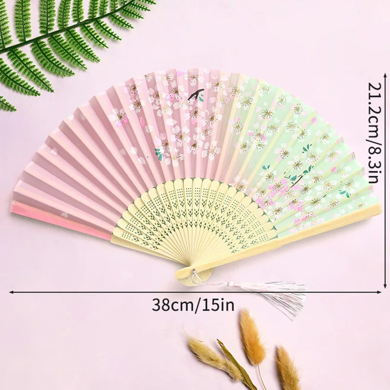A pink and green vintage lace folding hand fan with a durable handle displayed on a light purple background.