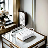 A white ultra-thin power strip with six outlets and four USB ports is placed on a glass cabinet top next to a wall outlet.