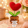 A handmade crochet heart plant with green leaves and a brown pot, displayed on a pink knitted surface.