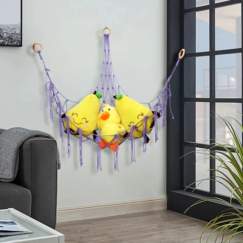 A yellow plush toy storage hammock with purple strings is hanging on a wall.
