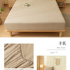 A beige fitted sheet is displayed on a wooden bed frame with natural light and decorative elements.