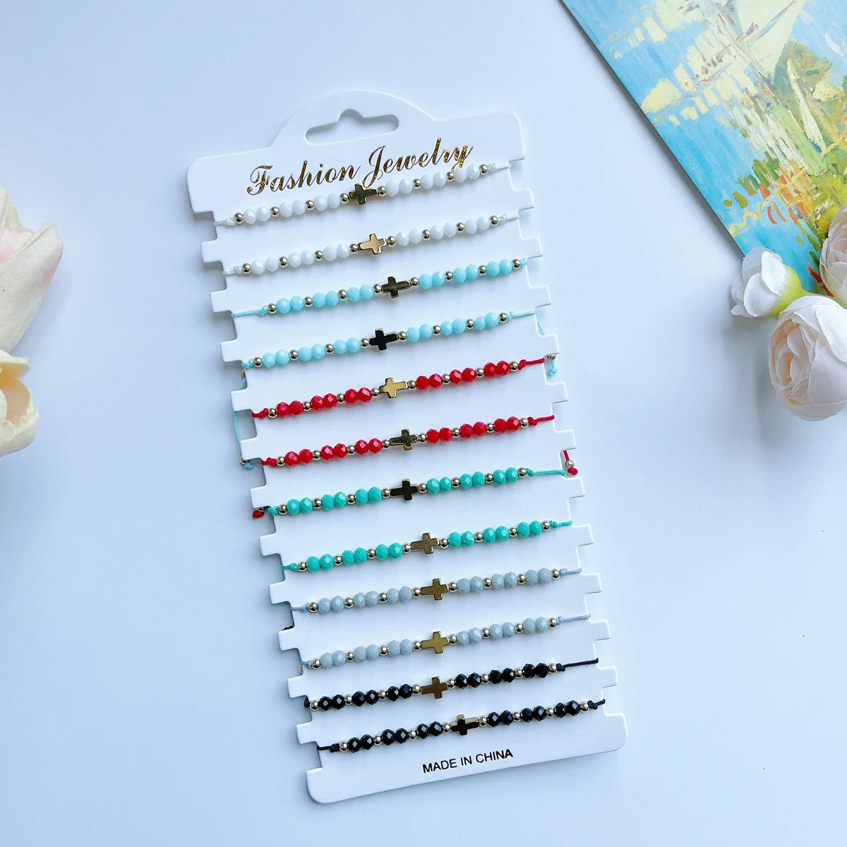 Présentation de bracelets de bijouterie en perles avec des croix dans des tons de blanc, bleu, rouge et noir.