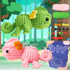 A beginner crochet kit featuring a green frog amigurumi and a pink hedgehog, along with yarn and tools.